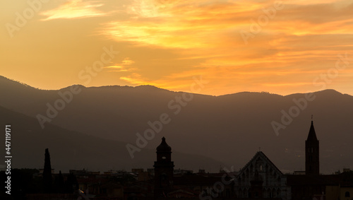 The rooftops and church towers of Pisa, Italy, silhouetted by a beautiful sunrise, with the mountains in the background