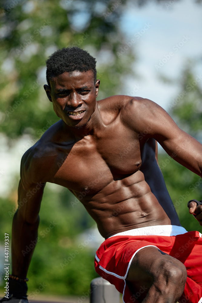 Muscular young man exercising at the sports field. African man looking to the side while doing horizontal bar exercises. Shirtless male model exercising outdoors. Muscular young man exercising at the sports field. African man looking to the side while doing horizontal bar exercises. Shirtless male model exercising outdoors.