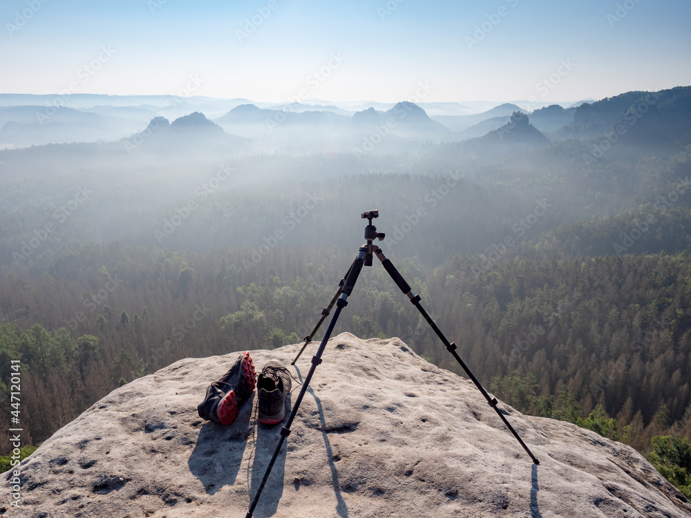 Modern professional travel tripod and black red sneakers on mountain summit.