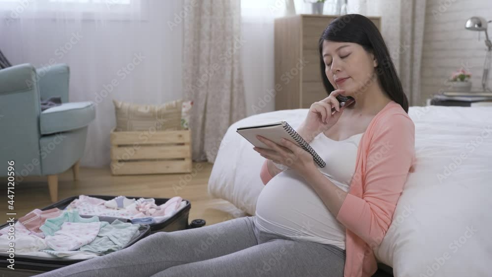 pregnant mom is looking into the distance and touching her chin in contemplation while adding details to the shopping list for baby accessories at home. pregnant mom is looking into the distance and touching her chin in contemplation while adding details to the shopping list for baby accessories at home.