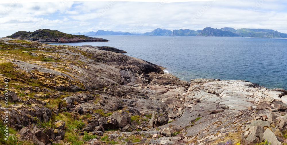 Rocky shore panorama view on the fjord stone coastline Lofoten islands, Norway under cloudy sky and mountains at horizon line.