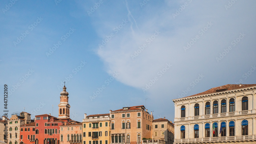Tower over colorful Venetian houses under blue sky, Venice, Italy