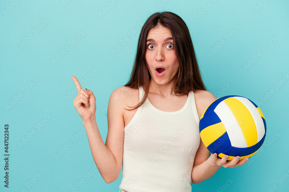 Young caucasian woman playing volleyball isolated on blue background pointing to the side