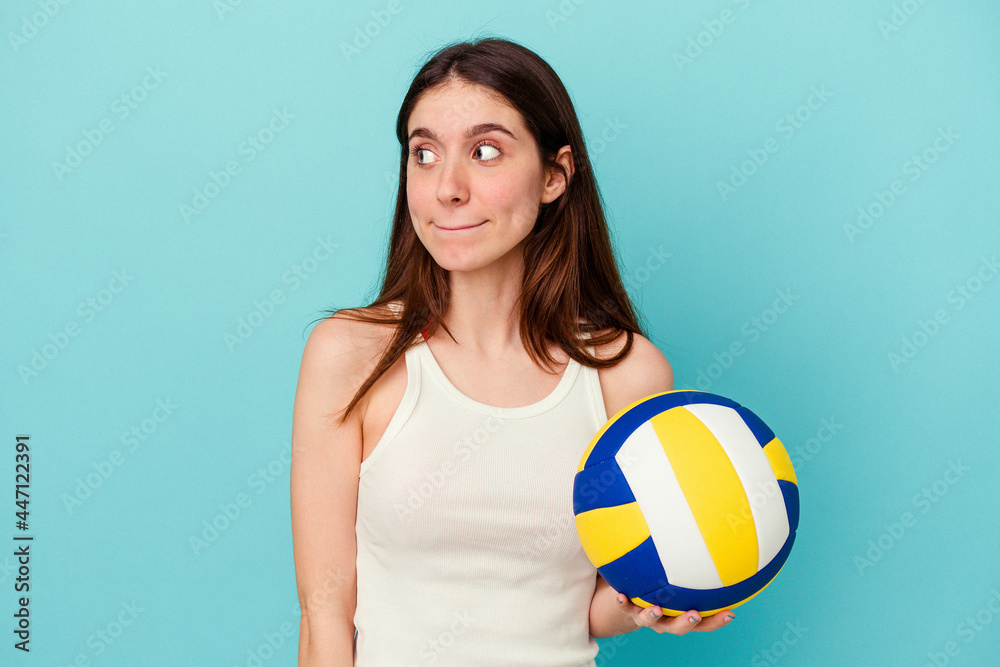 Young caucasian woman playing volleyball isolated on blue background confused, feels doubtful and unsure. Young caucasian woman playing volleyball isolated on blue background confused, feels doubtful and unsure.