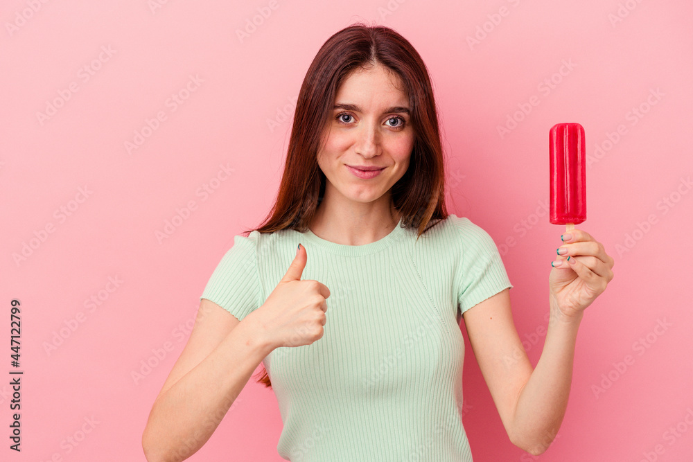 Young caucasian woman holding an ice cream isolated on blue background smiling and raising thumb up Young caucasian woman holding an ice cream isolated on blue background smiling and raising thumb up