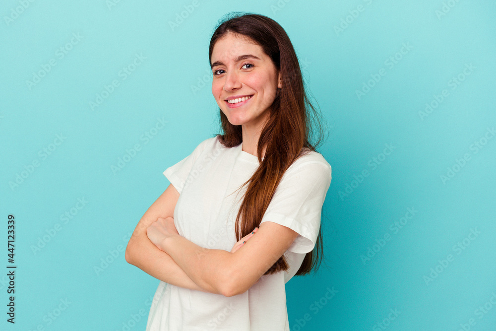 Young caucasian woman isolated on blue background who feels confident, crossing arms with determination. Young caucasian woman isolated on blue background who feels confident, crossing arms with determination.