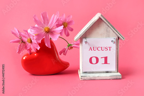 Calendar for August 1 : the name of the month of August in English with the numbers 0 and 1 on a toy house, a bouquet of pink flowers in a heart-shaped vase, a pink background photo