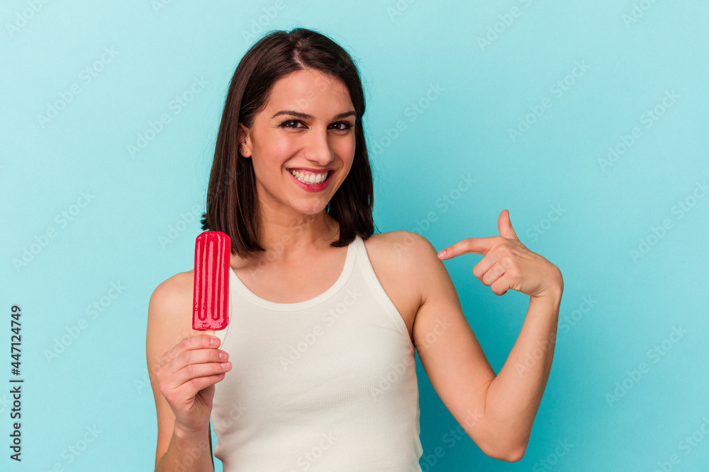 Young caucasian woman holding an ice cream isolated on blue background person pointing by hand to a shirt copy space, proud and confident Young caucasian woman holding an ice cream isolated on blue background person pointing by hand to a shirt copy space, proud and confident