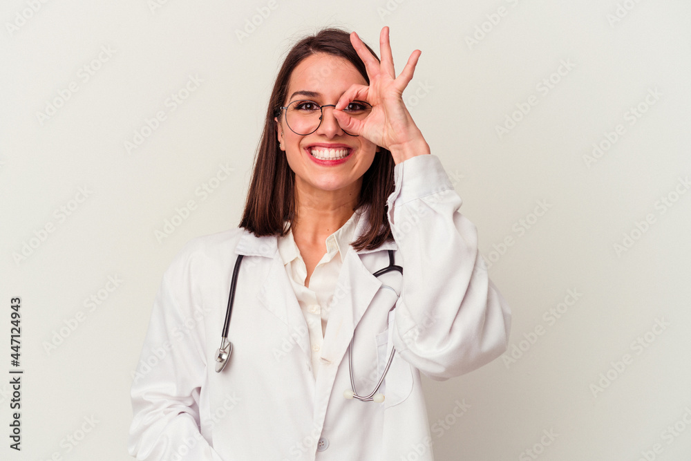 Young doctor caucasian woman isolated on white background excited keeping ok gesture on eye.