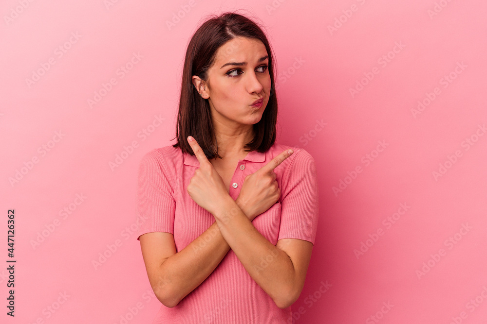 Young caucasian woman isolated on pink background points sideways, is trying to choose between two options. Young caucasian woman isolated on pink background points sideways, is trying to choose between two options.
