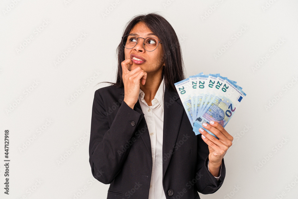 Young business latin woman holding bills isolated on white background relaxed thinking about something looking at a copy space. Young business latin woman holding bills isolated on white background relaxed thinking about something looking at a copy space.