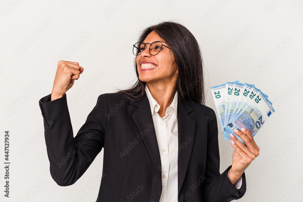 Young business latin woman holding bills isolated on white background raising fist after a victory, winner concept. Young business latin woman holding bills isolated on white background raising fist after a victory, winner concept.