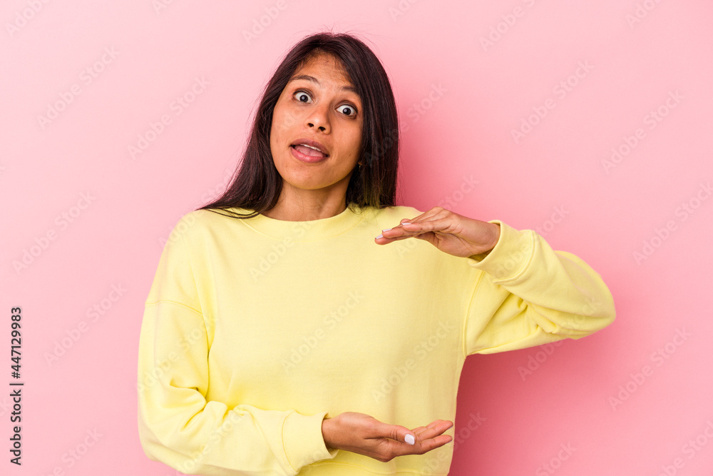 Fototapeta premium Young latin woman isolated on pink background holding something with both hands, product presentation.