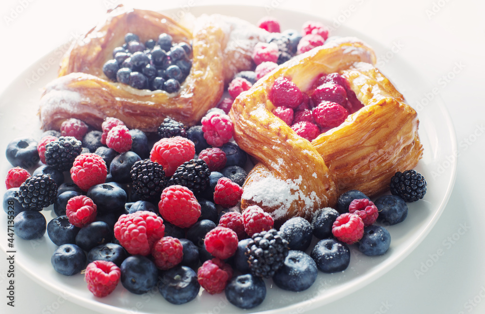 Danish with raspberries and blueberries on  round plate with berries on  white table