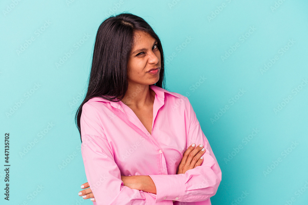 Young latin woman isolated on blue background frowning face in displeasure, keeps arms folded. Young latin woman isolated on blue background frowning face in displeasure, keeps arms folded.