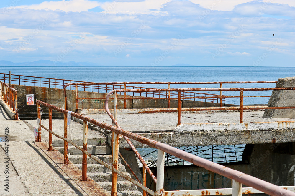 Remains of a rusted handrails on an abandoned waterfront on a blurred background of azure sea waves.