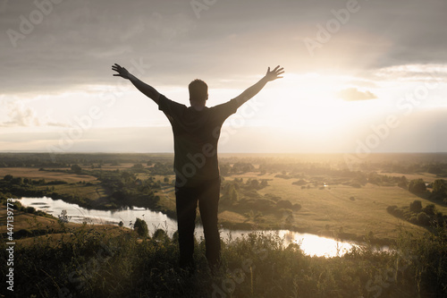 Silhouette of man standing with stretched out hands against the romantic sunset sky, concept of joy and happiness, arms up in praise to GodMotivation and Strength Concept.