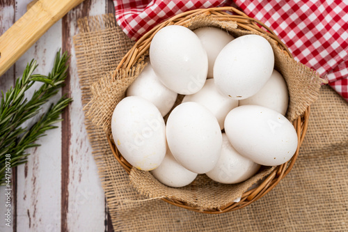 Overhead view of organic farm white eggs in a basket on a rustic wooden table with rosemary. photo