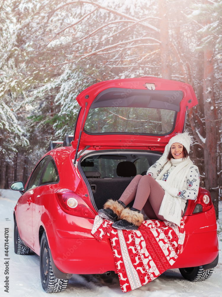 happy young pretty woman is sitting in the open trunk of car in the forest in winter, winter Christmas or New Year travel or vacation