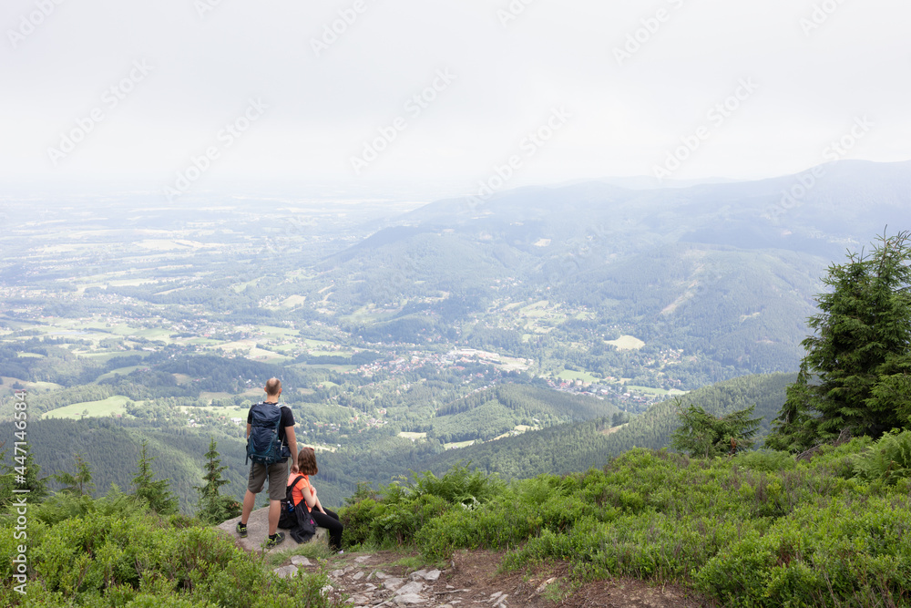 Couple of two tourists, backpackers, hikers and trippers are having a rest and looking from lookout and outlook. Smrk, Beskid mountains, Czech Republic, Czechia. People in the nature.