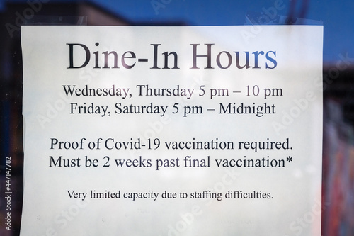 Sign in restaurant window during time of Covid stating proof of vaccination is required for dining and that the restaurant is understaffed due to hiring difficulties. photo
