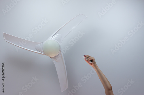 Close-up of hand holding remote control of white ceiling fan. Hand turning on the fan with copy space for text. photo