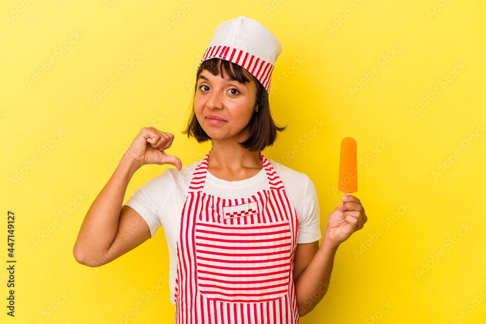 Young mixed race ice cream maker woman holding an ice cream isolated on yellow background feels proud and self confident, example to follow. Young mixed race ice cream maker woman holding an ice cream isolated on yellow background feels proud and self confident, example to follow.