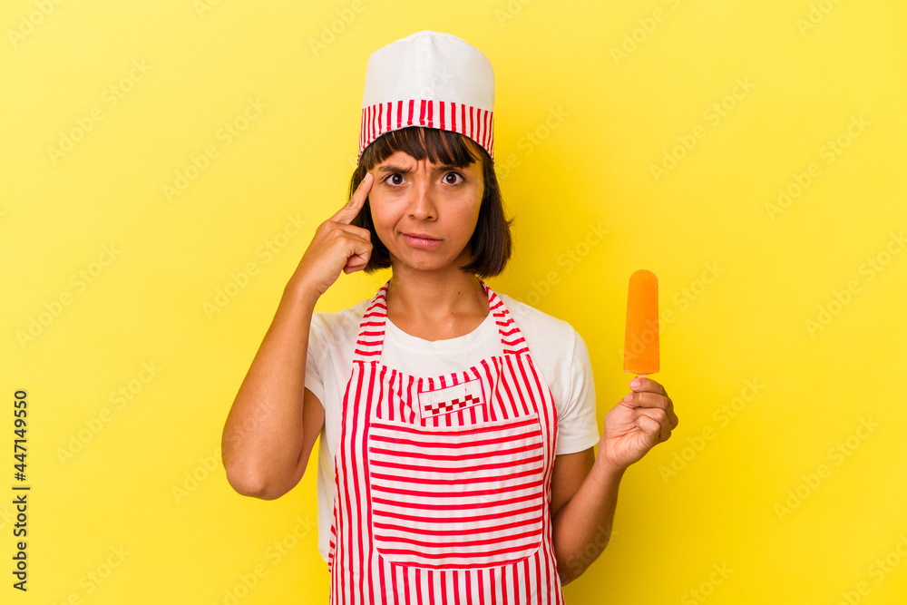 Young mixed race ice cream maker woman holding an ice cream isolated on yellow background pointing temple with finger, thinking, focused on a task.