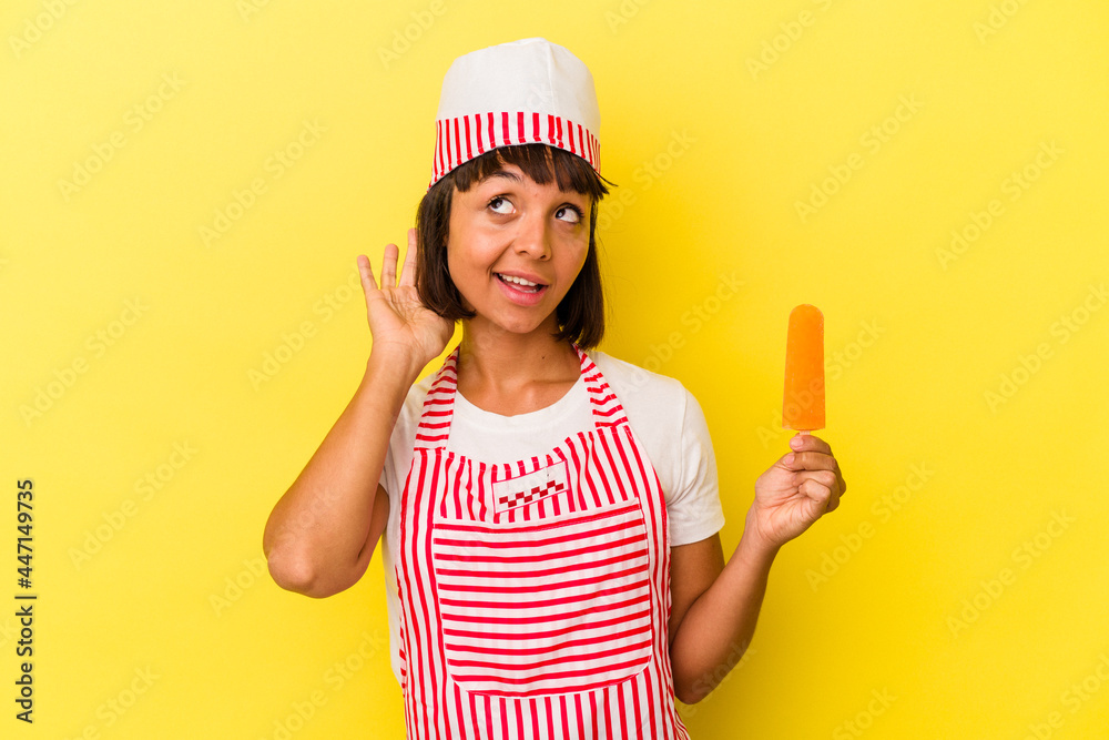 Young mixed race ice cream maker woman holding an ice cream isolated on yellow background trying to listening a gossip. Young mixed race ice cream maker woman holding an ice cream isolated on yellow background trying to listening a gossip.