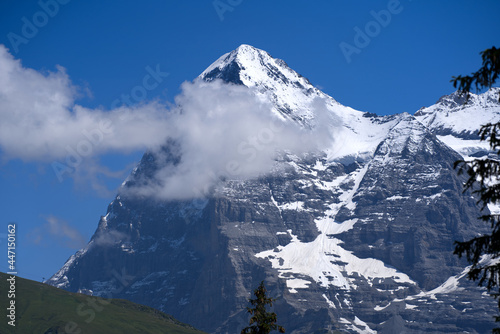 Mountain peak Eiger at Bernese highland on a sunny summer day with blue sky background and clouds in the foreground. Photo taken July 20th, 2021, Lauterbrunnen, Switzerland. © Michael Derrer Fuchs