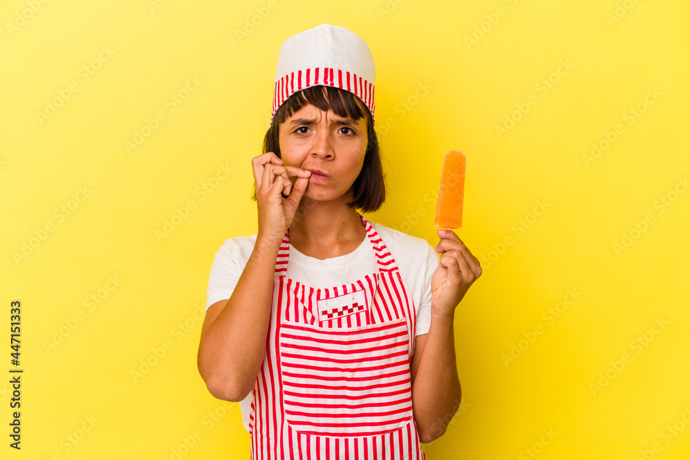 Young mixed race ice cream maker woman holding an ice cream isolated on yellow background with fingers on lips keeping a secret. Young mixed race ice cream maker woman holding an ice cream isolated on yellow background with fingers on lips keeping a secret.