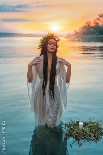 Pagan girl Slavic goddess emerges from water lake ritual flower wreaths float, candles burning. fashion model. Holiday Ivan Kupala. Fantasy woman enjoy summer sunset. Wet white vintage medieval dress photo