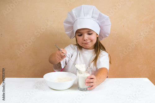 A little girl dressed as a cook kneads the dough. Cooking child lifestyle concept. The kid loves, has fun, studies and plays in the kitchen