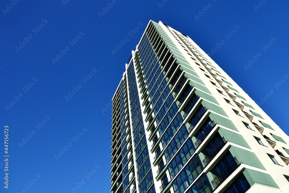 Facade of a new modern high-rise residential building. Skyscraper on blue sky background. Tall house renovation project, government programs. Minimalistic multi storied home.