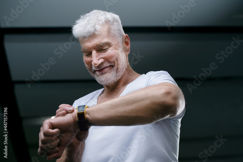 Handsome gray haired senior man looking at sport watch in his hand. Sport and health care concept