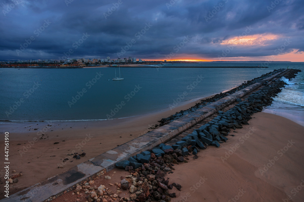 Pier to famous old farol de Portimao molhe este under gloomy sunset.