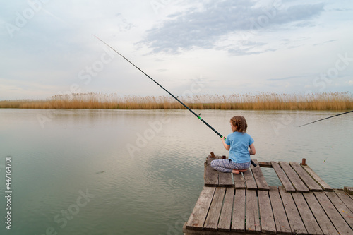 fisherman. little girl sits on a wooden bridge on a river with fishing rod.