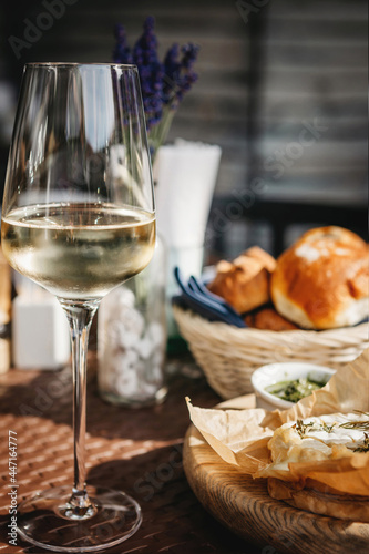 Glass of cold white wine and oven baked camembert cheese with rosemary on baking paper on wooden plate. Serving lunch at the winery, rustic style table setting