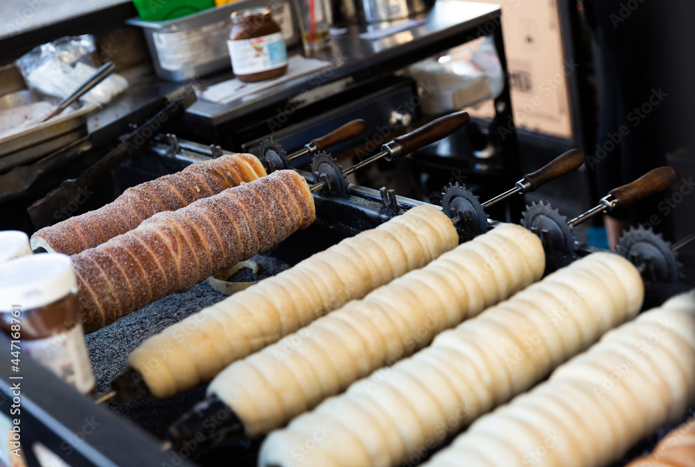 Traditional cooking of Czech trdelnik on street market - yeast rolled dough wrapping around stick and baking on grill
