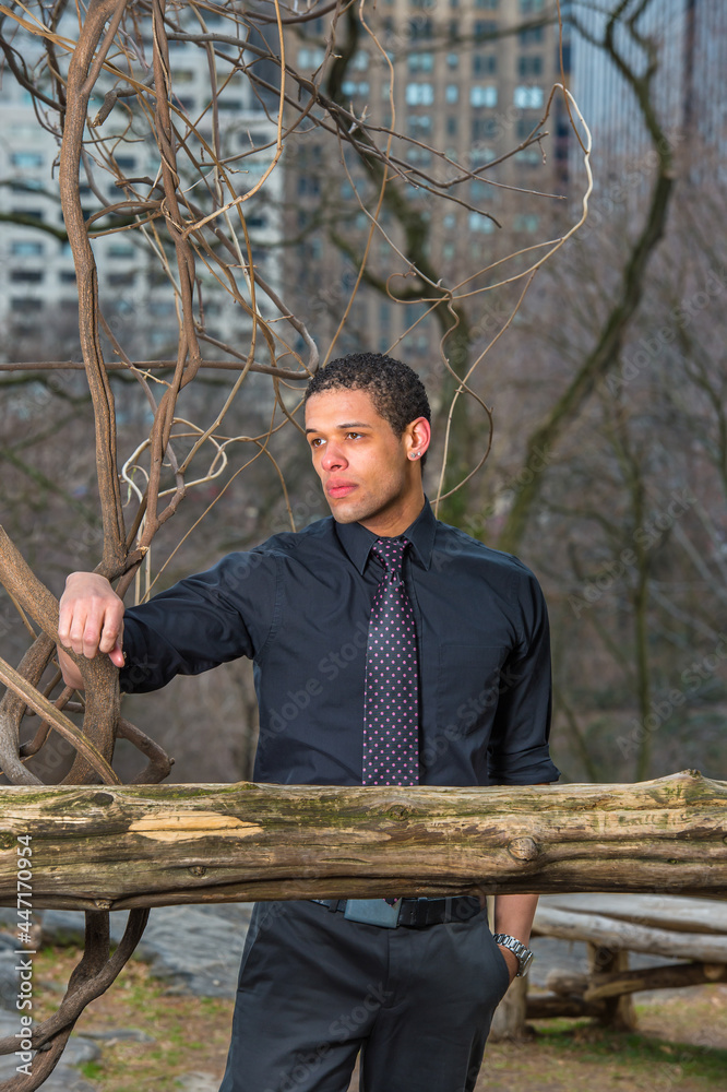 Fototapeta premium Dressing in a black shirt, tie, a young handsome guy is pondering at small woods in winter.