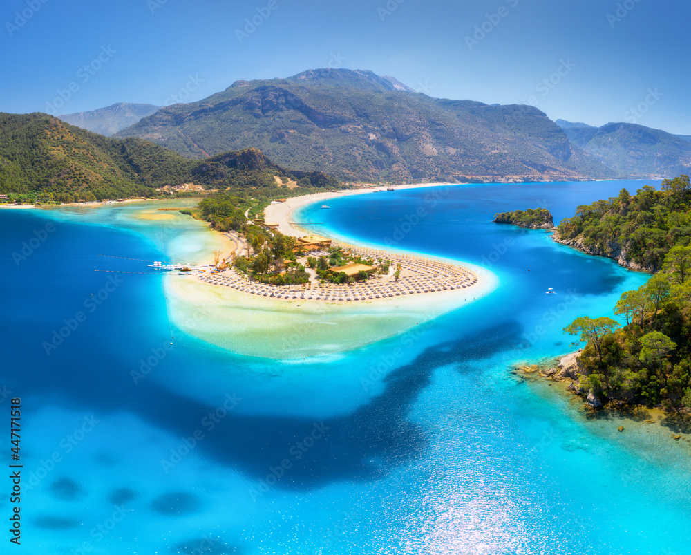 Aerial view of sea bay, sandy beach with umbrellas, trees, mountain at sunny day in summer. Blue lagoon in Oludeniz, Turkey. Tropical landscape with white sandy bank, blue water. View from above