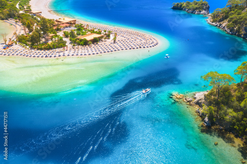 Aerial view of sandy beach  blue sea  speed boat at sunny day in summer. Motorboat in Blue Lagoon  sun beds  clear azure water. Tropical landscape with yacht  green trees. Top view. Oludeniz  Turkey