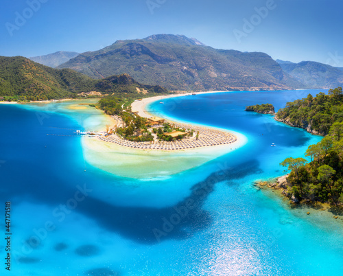 Aerial view of sea bay, sandy beach with umbrellas, trees, mountain at sunny day in summer. Blue lagoon in Oludeniz, Turkey. Tropical landscape with white sandy bank, blue water. View from above