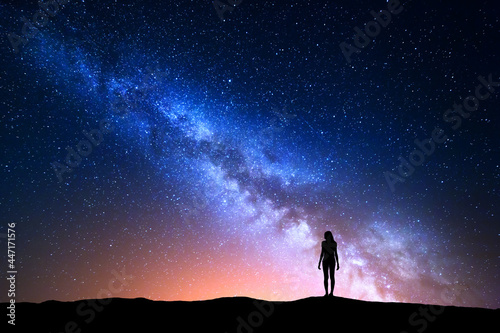 Beautiful Milky Way with standing woman. Colorful landscape with night sky with stars and silhouette of a girl on hill on the background of beautiful galaxy. Blue milky way with yellow light. Space