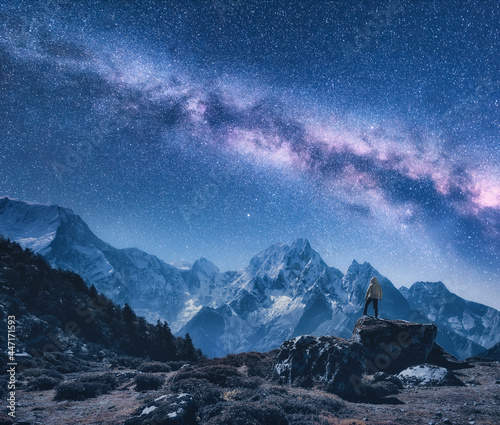 Silhouette of a standing man on the stone, mountains and starry sky with Milky Way at night in Nepal. Sky with stars. Travel. Night landscape with snow-covered rocks and purple milky way. Space