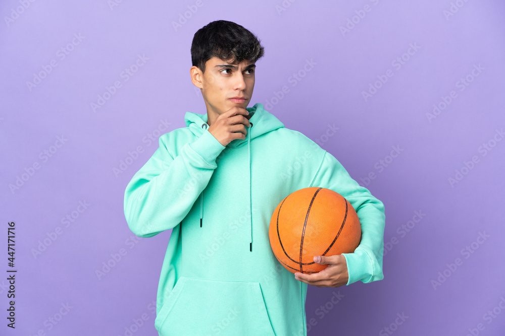 Young man playing basketball over isolated purple background and looking up