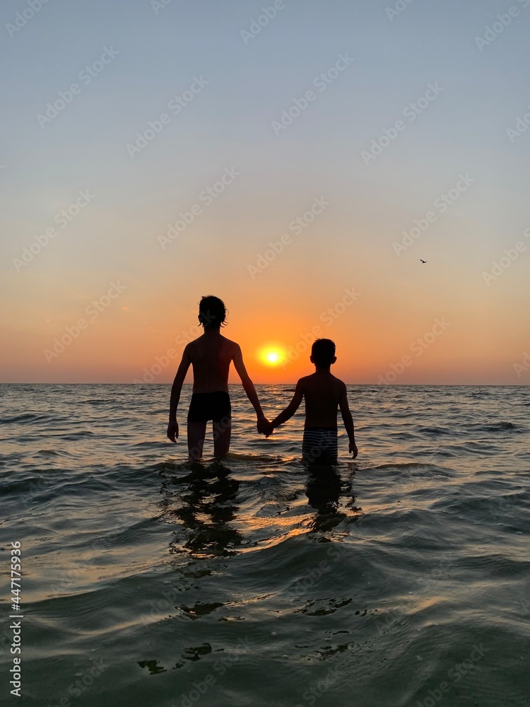 Children hold hands standing in the sea against the sunset. Children's rest on the beach at the sea. The boys are swimming in the sea.