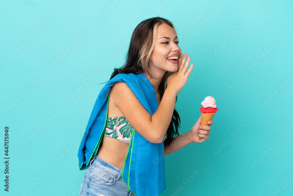 Teenager caucasian girl holding ice cream and towel isolated on blue background shouting with mouth wide open to the side