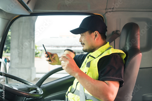 Cheerful men truck driver holding a cup of coffee and using smartphone