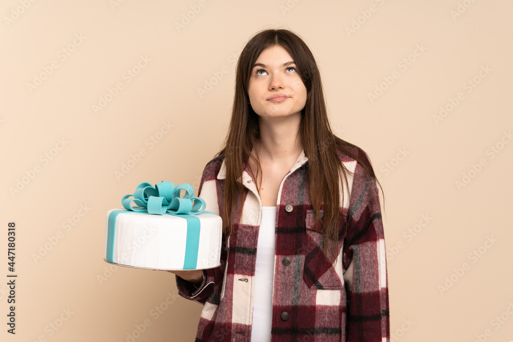 Young Ukrainian girl holding a big cake isolated on beige background and looking up Young Ukrainian girl holding a big cake isolated on beige background and looking up